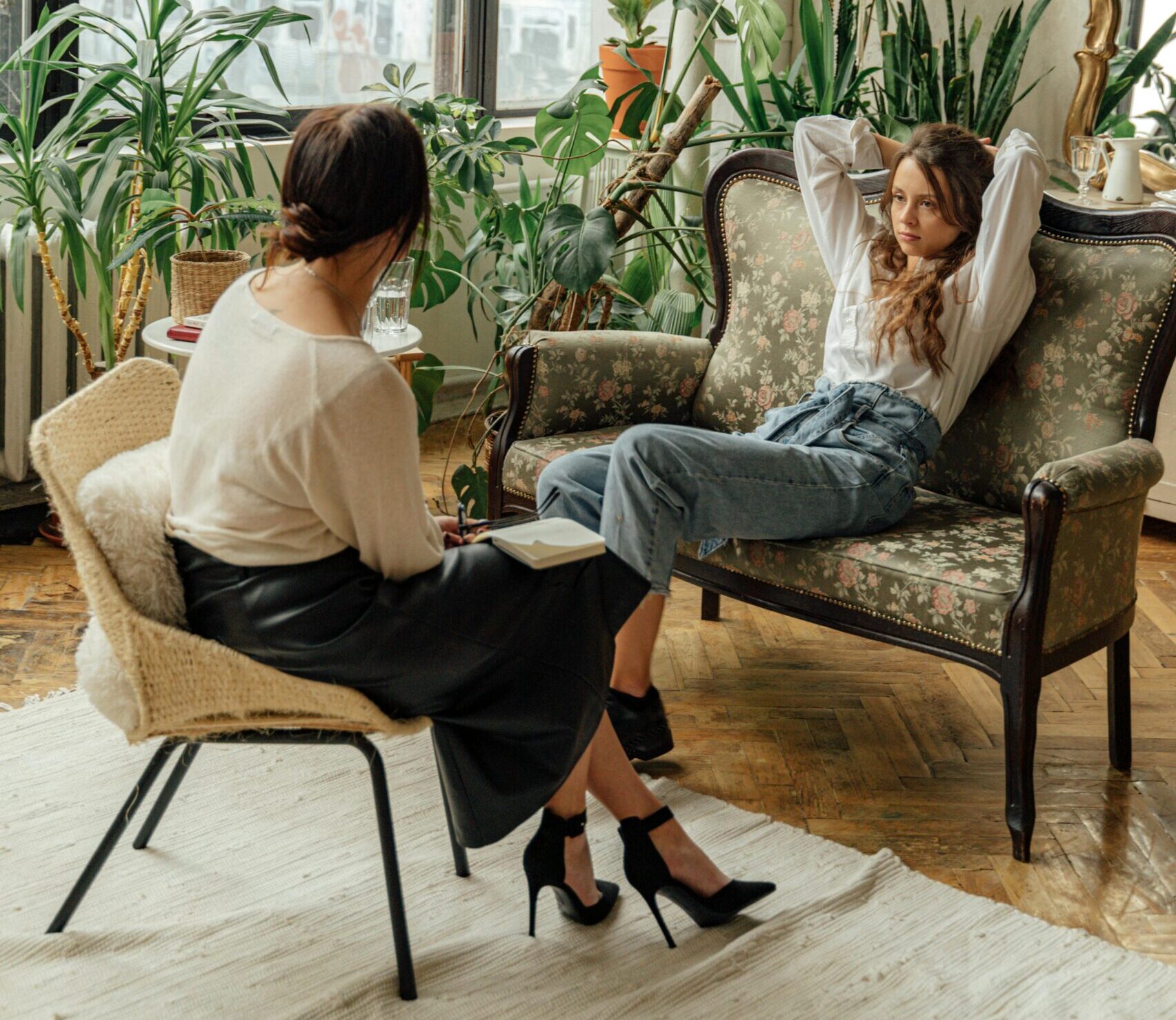 Two women engaged in a counseling session in a cozy, plant-filled living room.